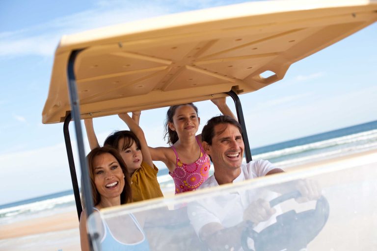 Family riding in a golf cart next to the beach.